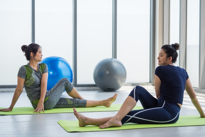 Two asian women doing yoga together at a gym.
