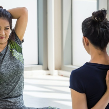 Two asian women doing yoga together at a gym.